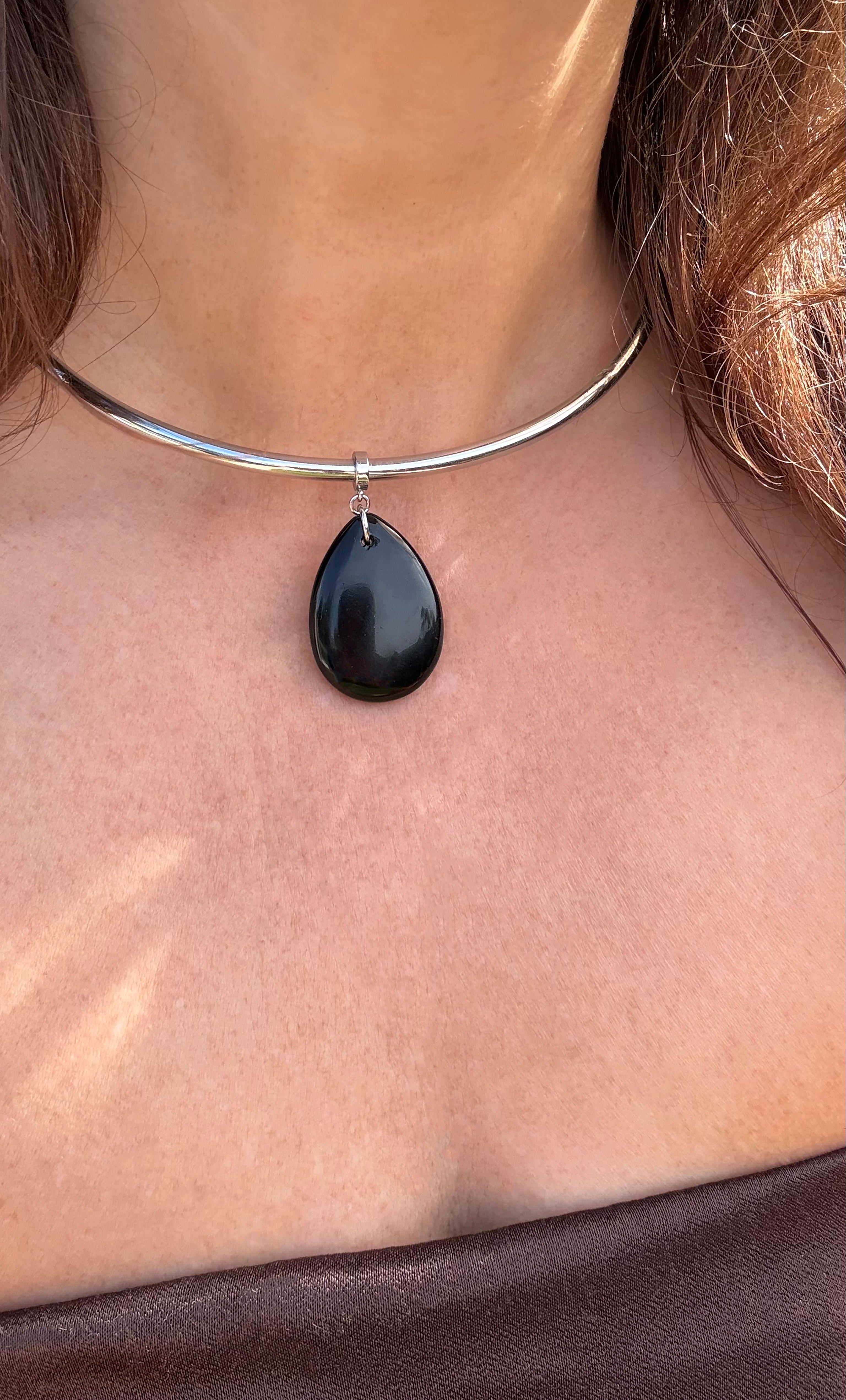 Silver collar necklace with a polished black teardrop agate pendant on a woman’s neck.