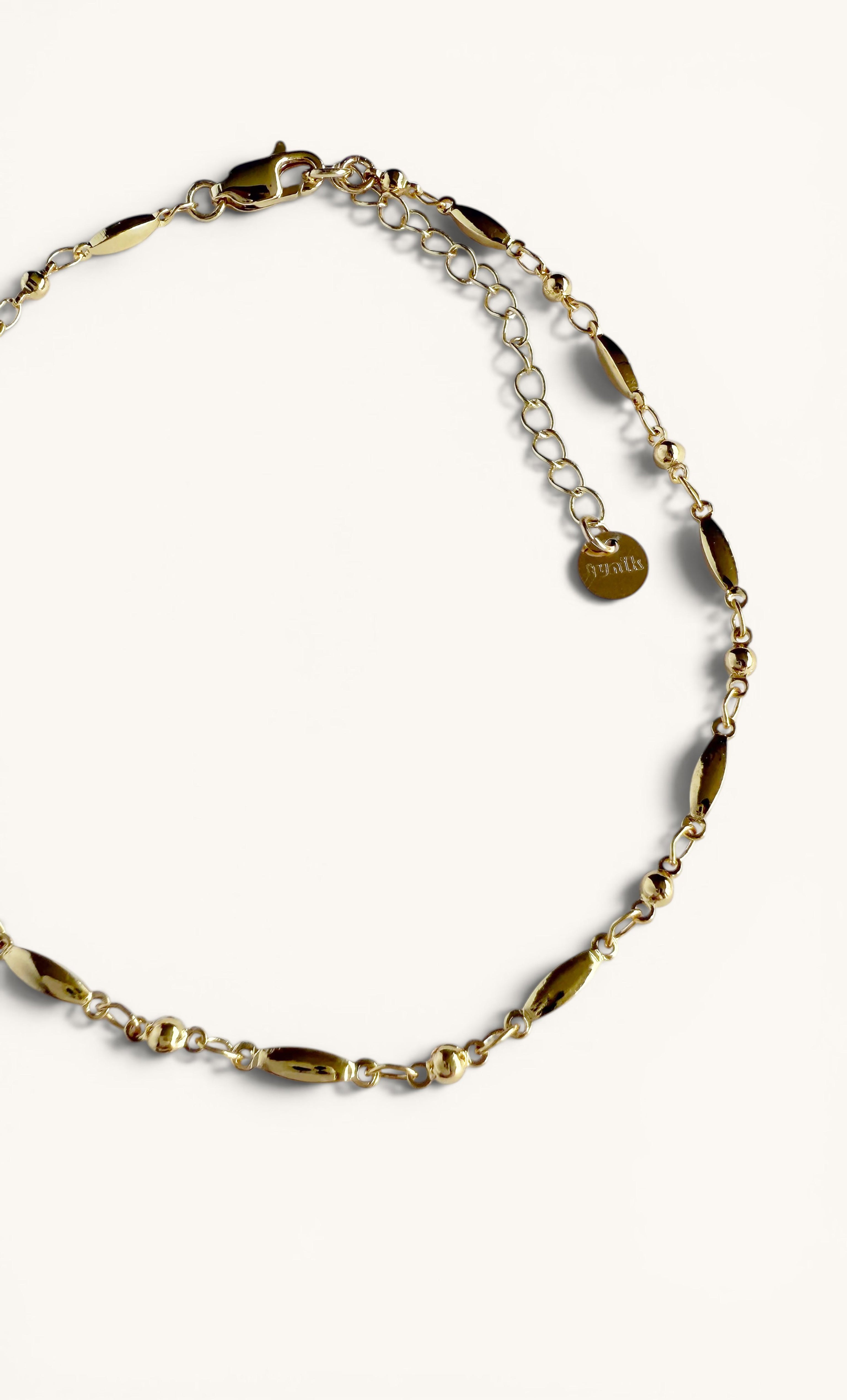 Delicate 24K gold fill beaded cable chain anklet with small round charms and Tunik logo tag.