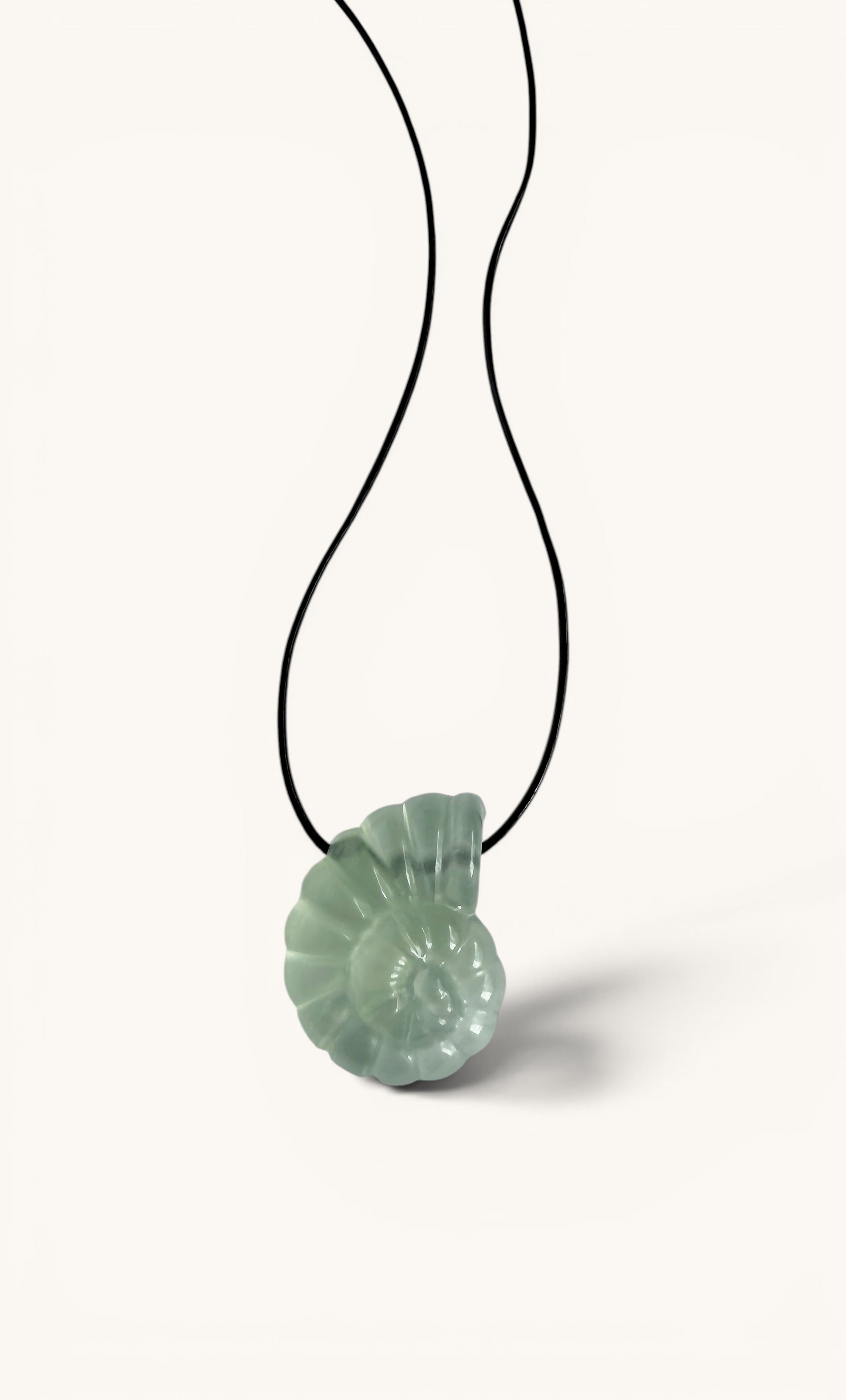 Green carved nautilus fluorite shell pendant on black cord necklace against white background.