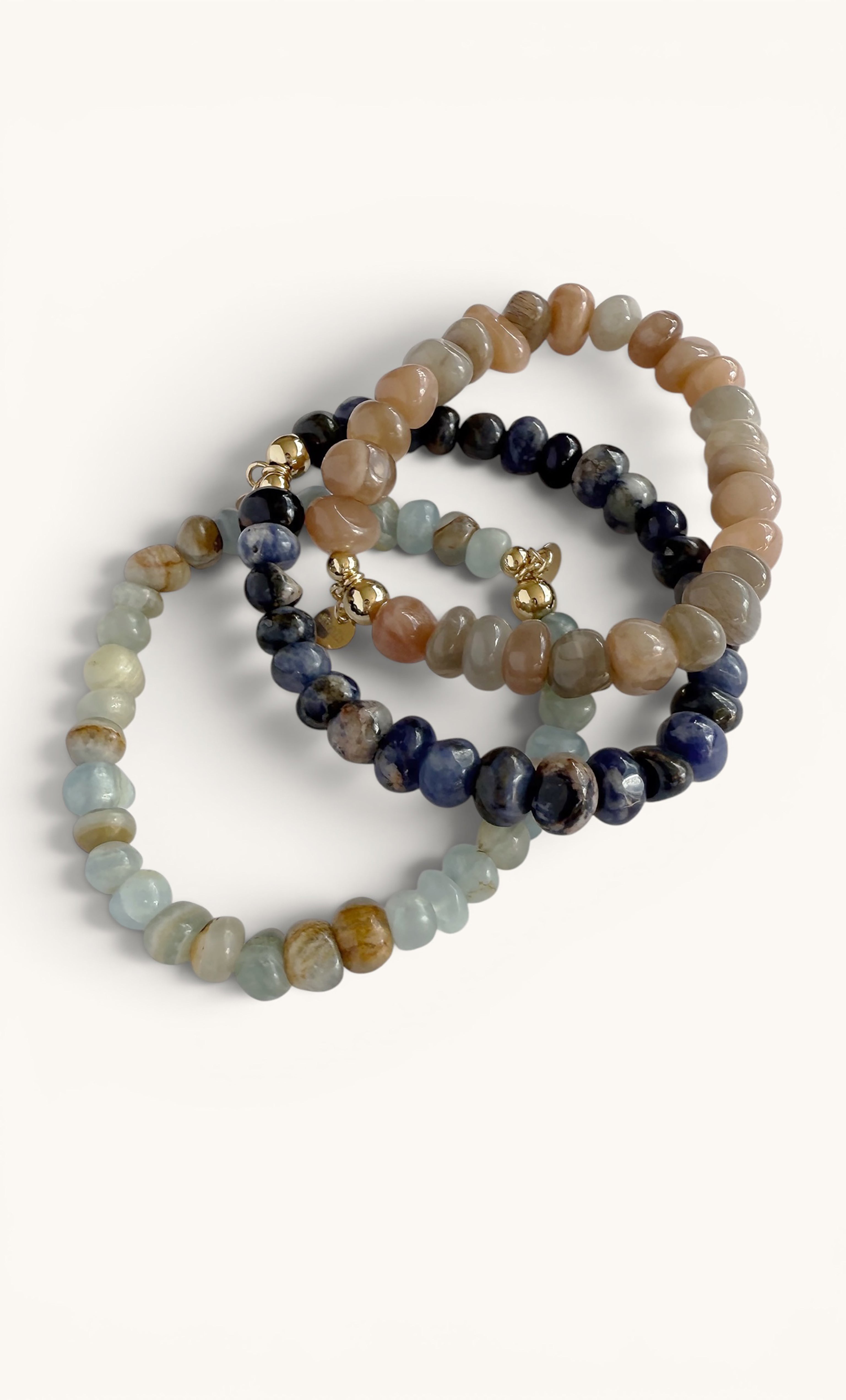 Set of three stretchy beaded bracelets featuring peach moonstone, navy blue, and light aqua stones with gold fill accents.