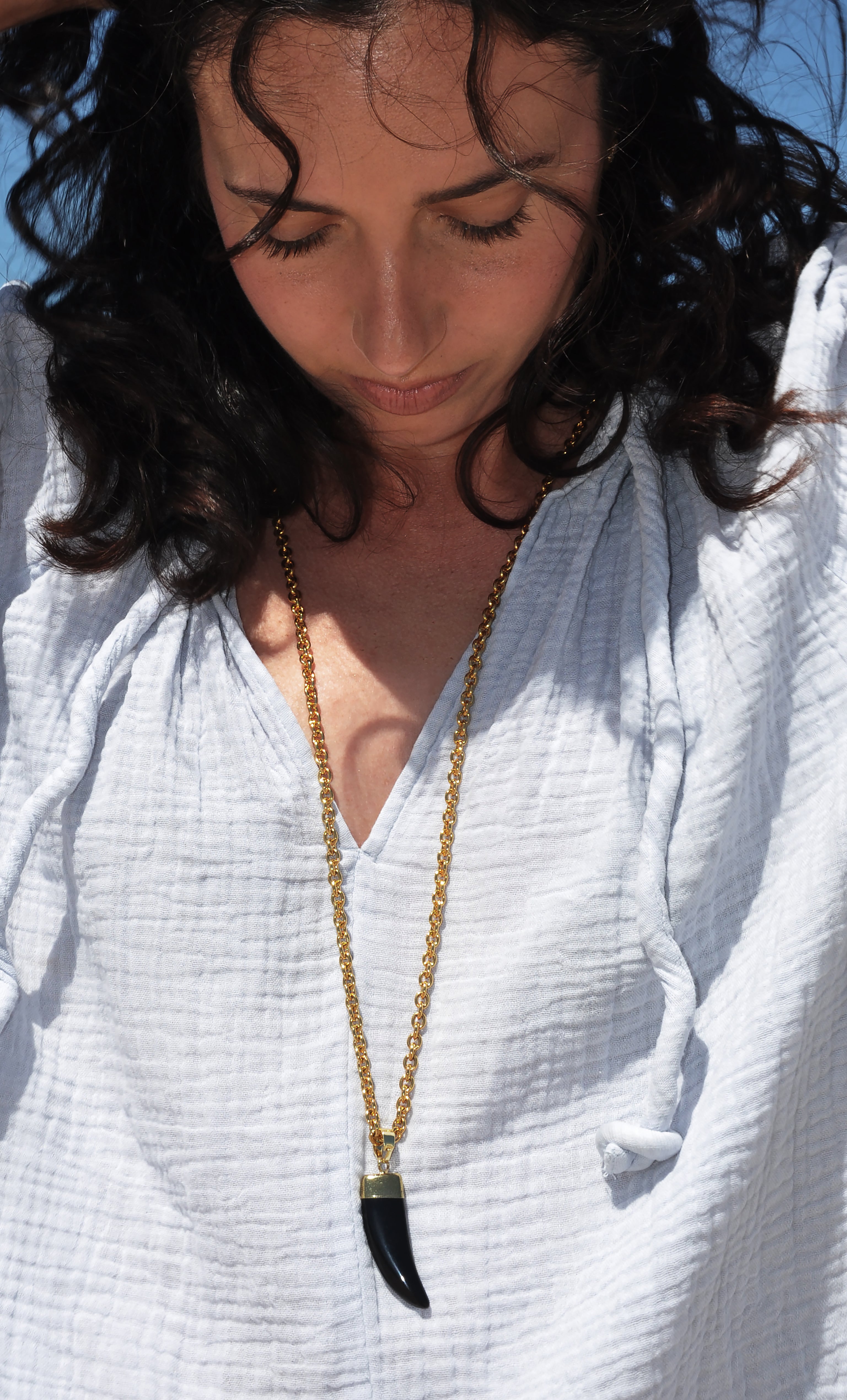 Long gold fill Tunik necklace with carved agate horn pendant worn over white textured top.