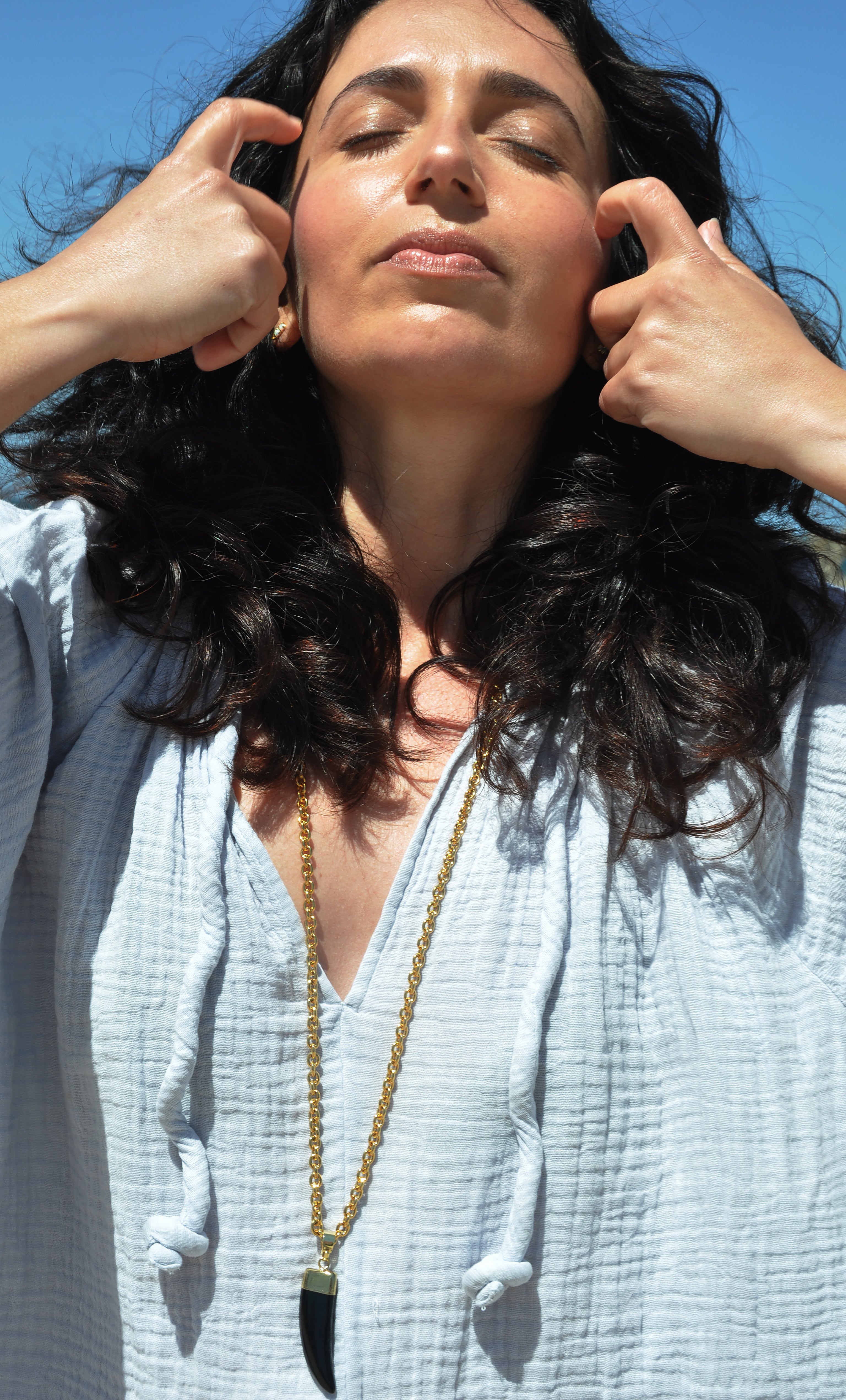 Tunik gold fill necklace with carved agate stone horn pendant on model against blue sky.