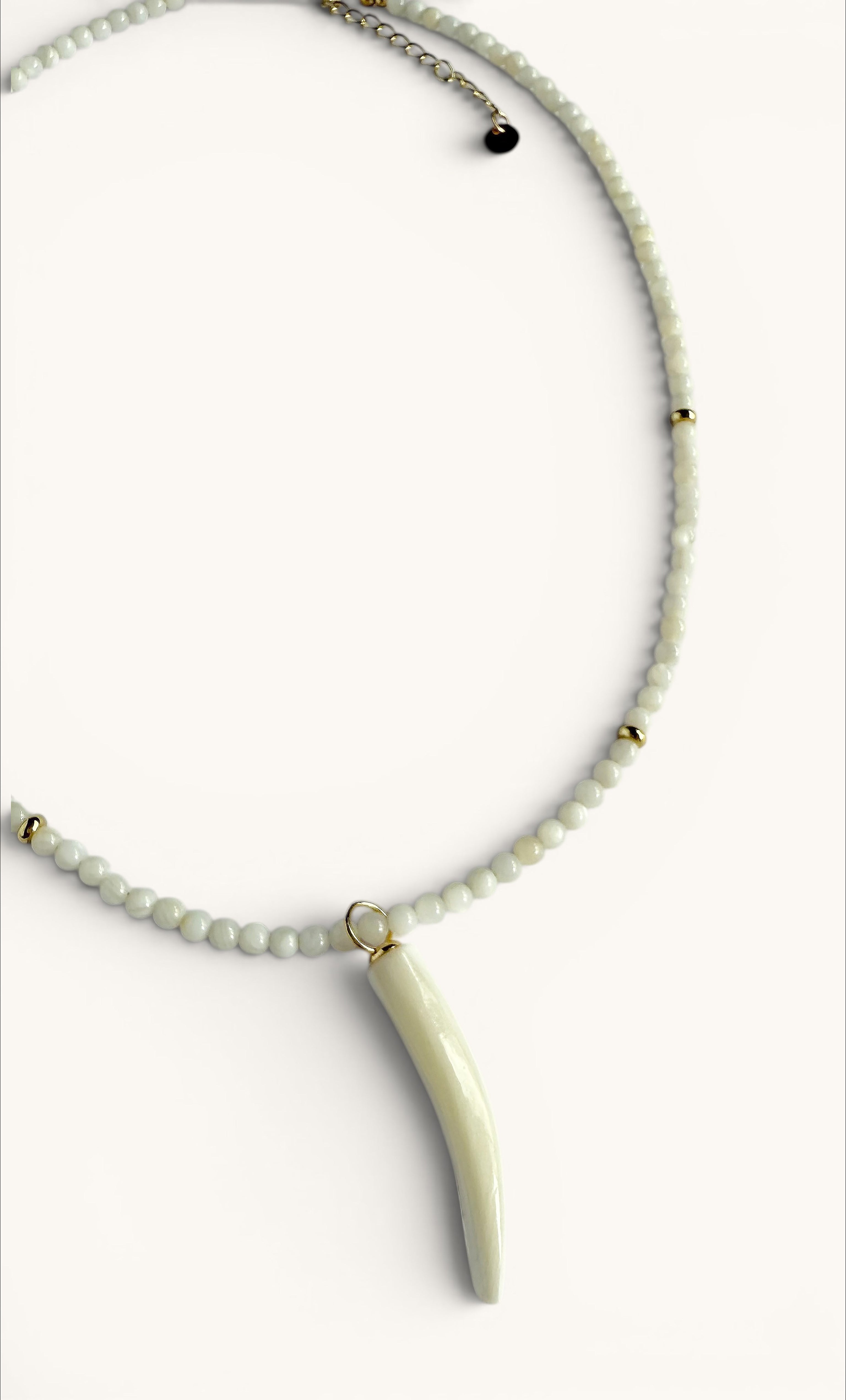 Delicate hand-beaded necklace with small white beads and gold accents, featuring a carved mother of pearl horn charm on a.