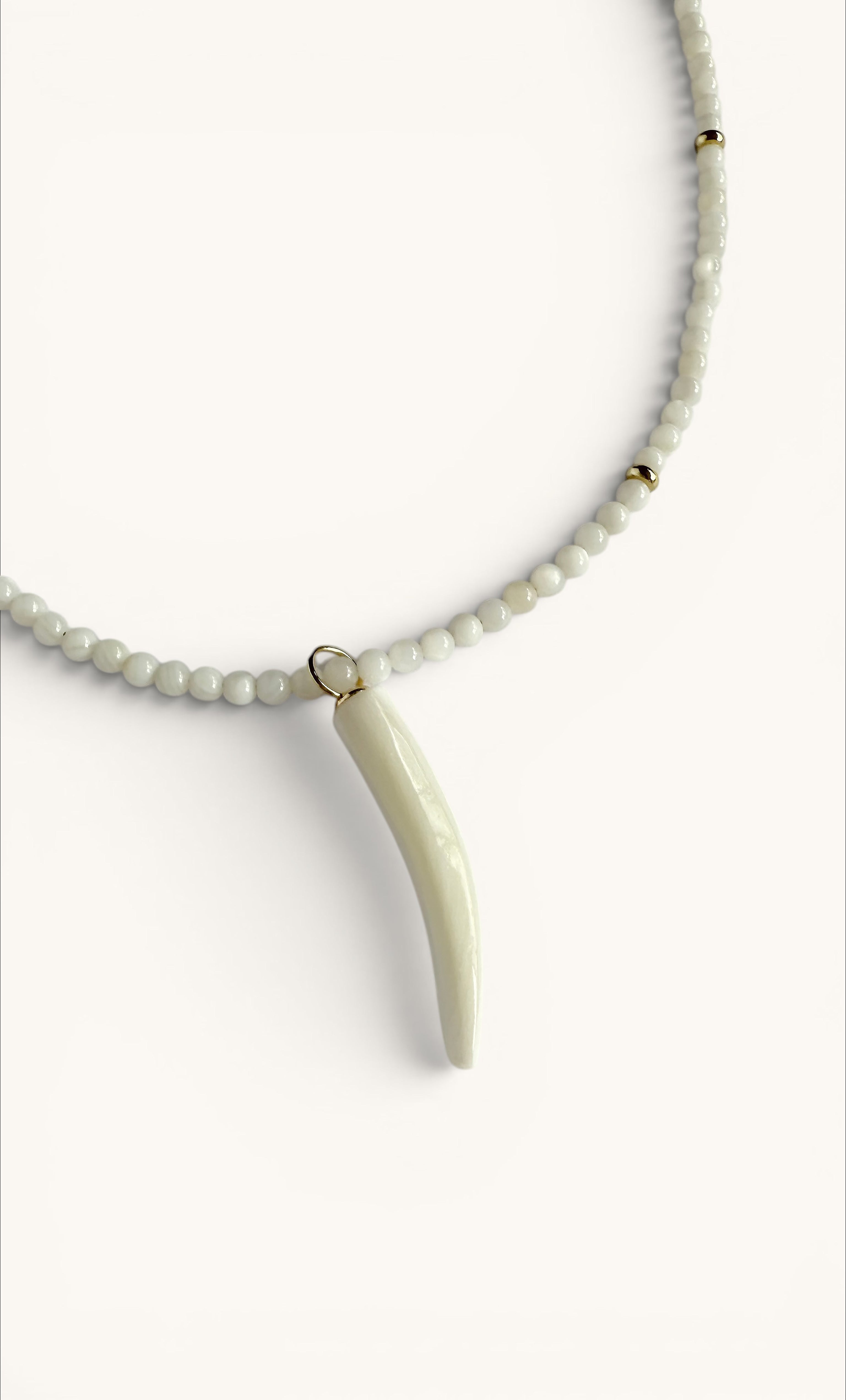 Gold fill necklace with small white beads and a carved mother of pearl horn charm by Tunik.