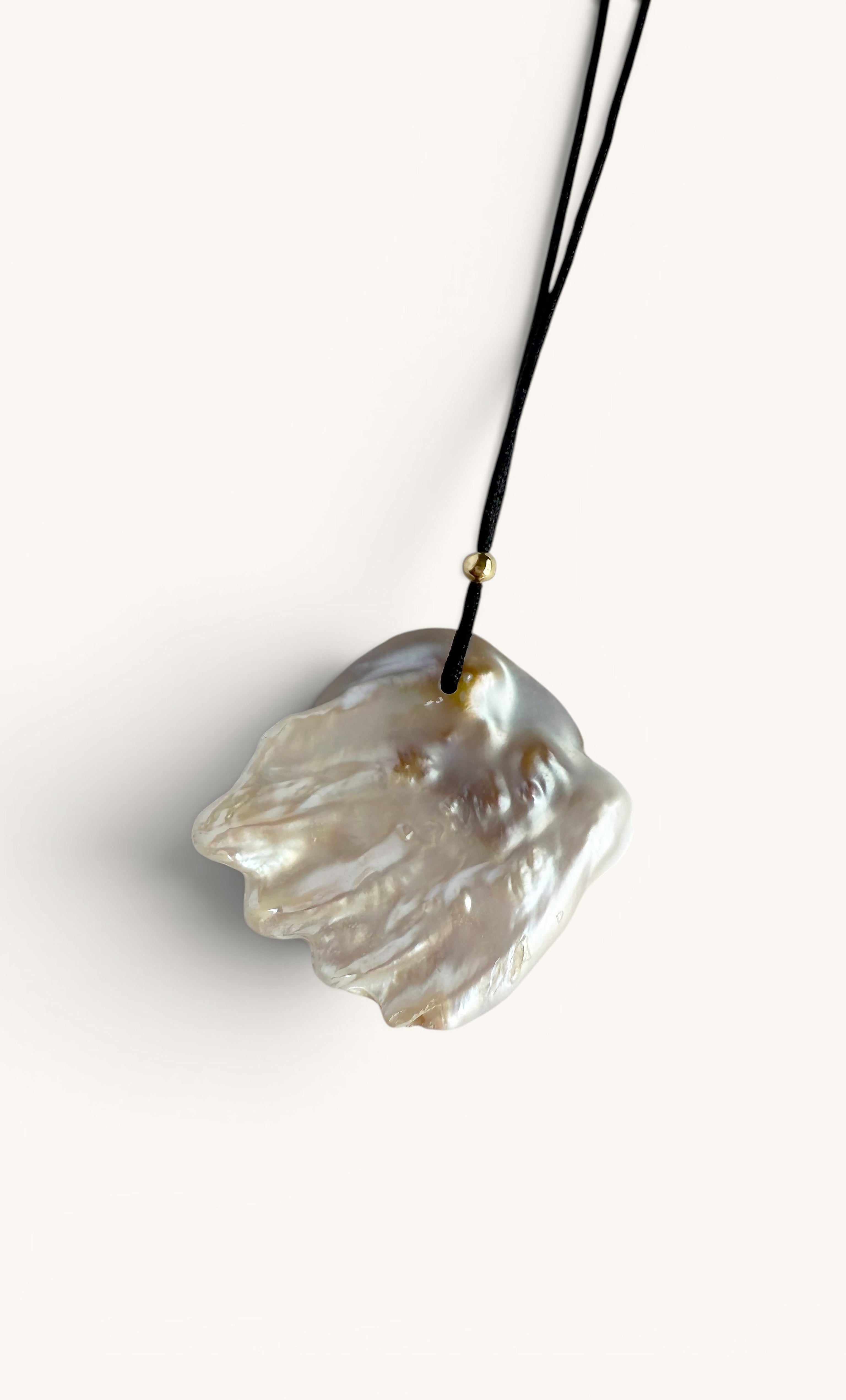 Long gold-fill necklace with a large irregular shaped freshwater blister pearl pendant on a black cord.