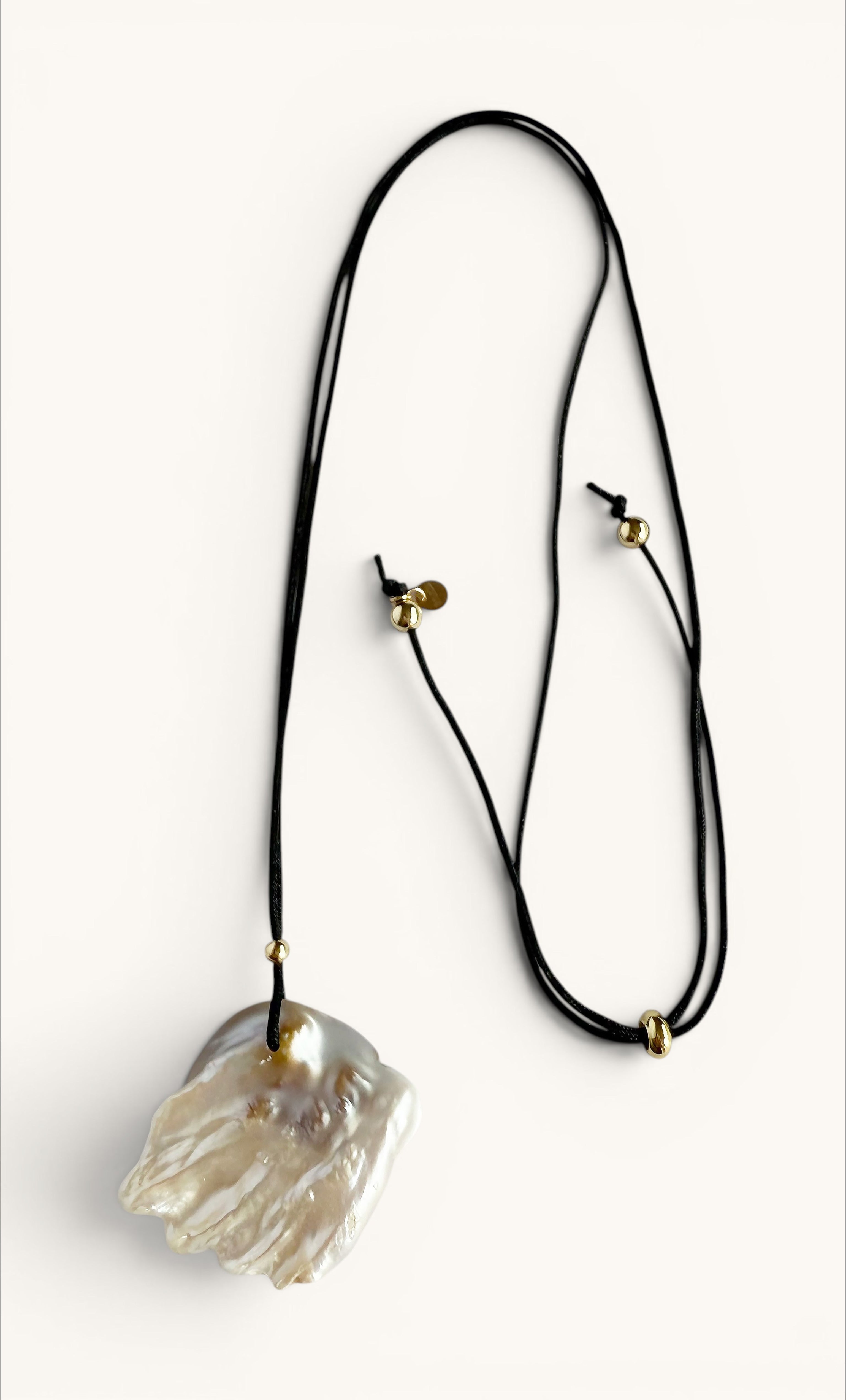 Gold-filled long line necklace with irregular freshwater blister pearl pendant on black cord.