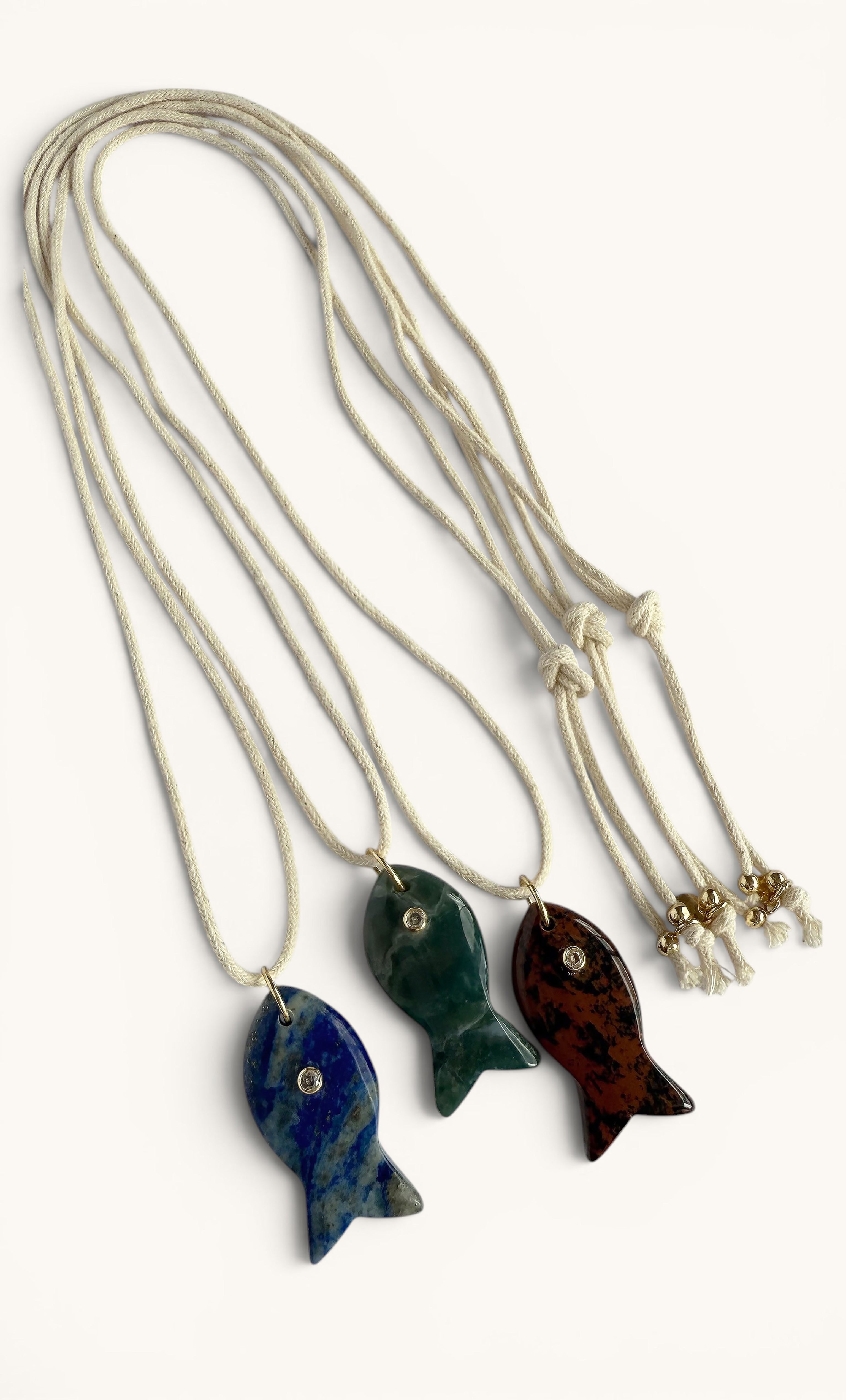 Three gold fill long line necklaces each featuring a carved fish pendant in green, blue, and brown apatite stone.
