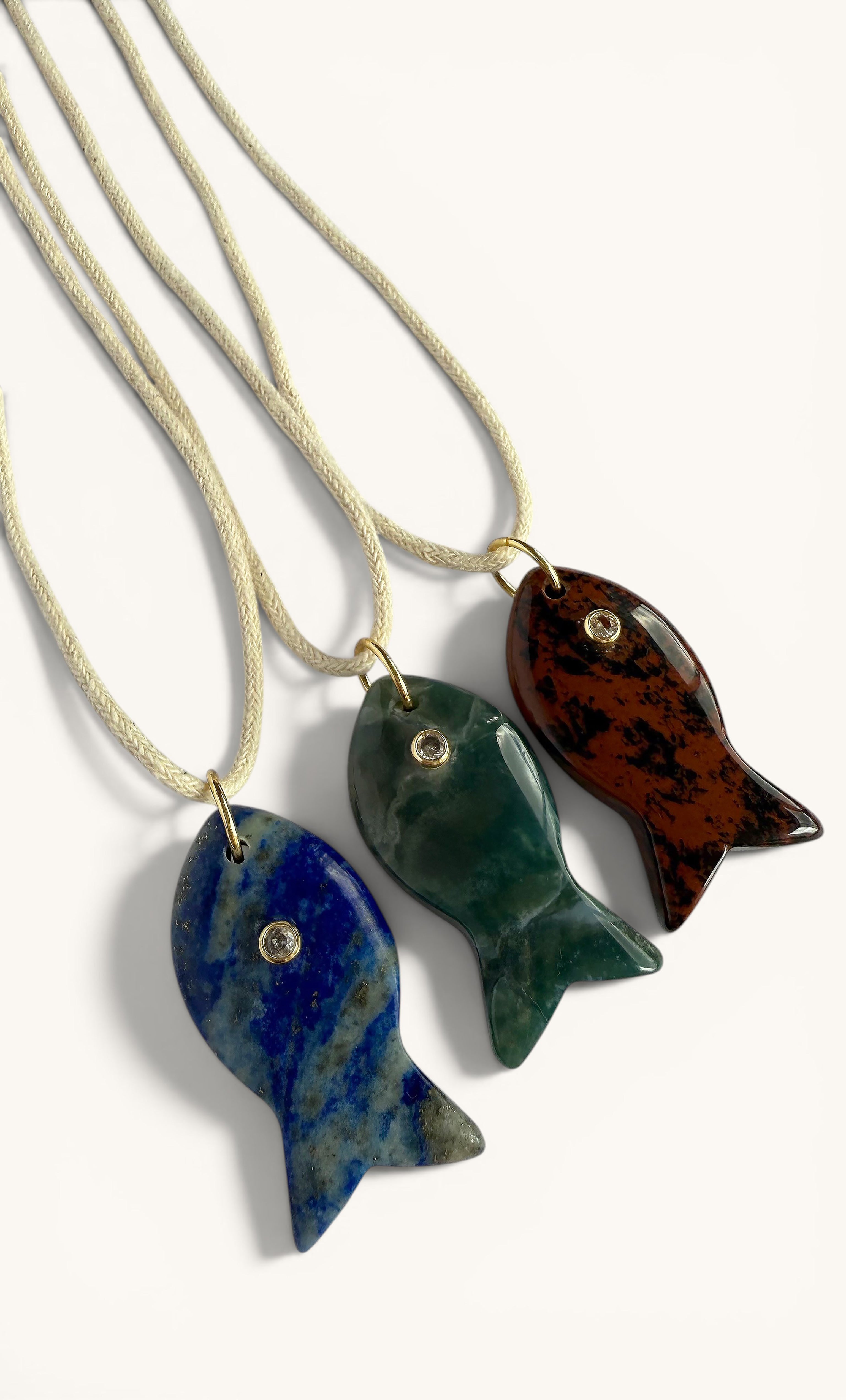 Three gold-filled long line necklaces each featuring a carved stone fish pendant in blue, green, and brown unique mottled.