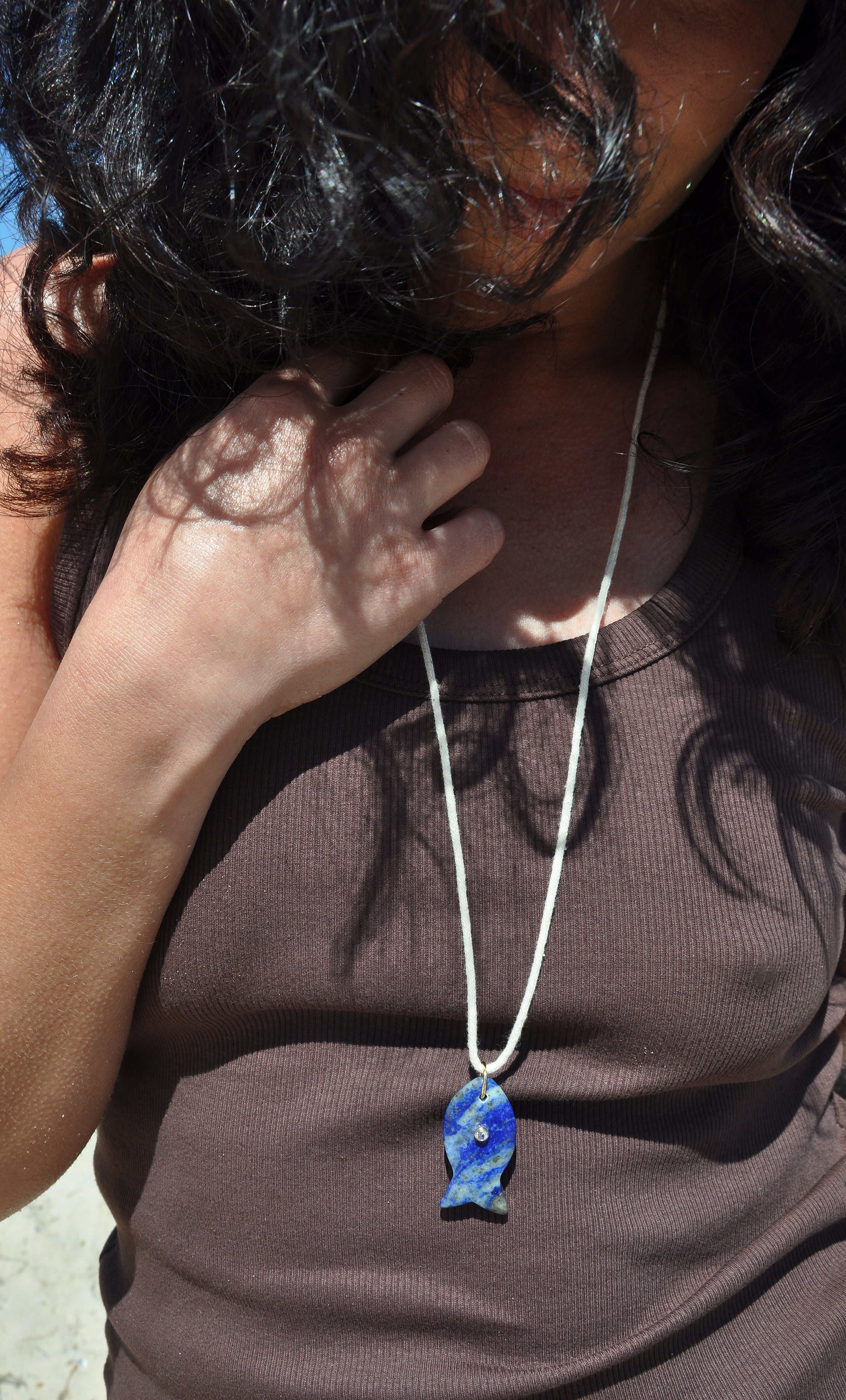 Gold fill long line necklace by Tunik the Label featuring a carved lapis lazuli stone fish pendant, styled with brown top,.