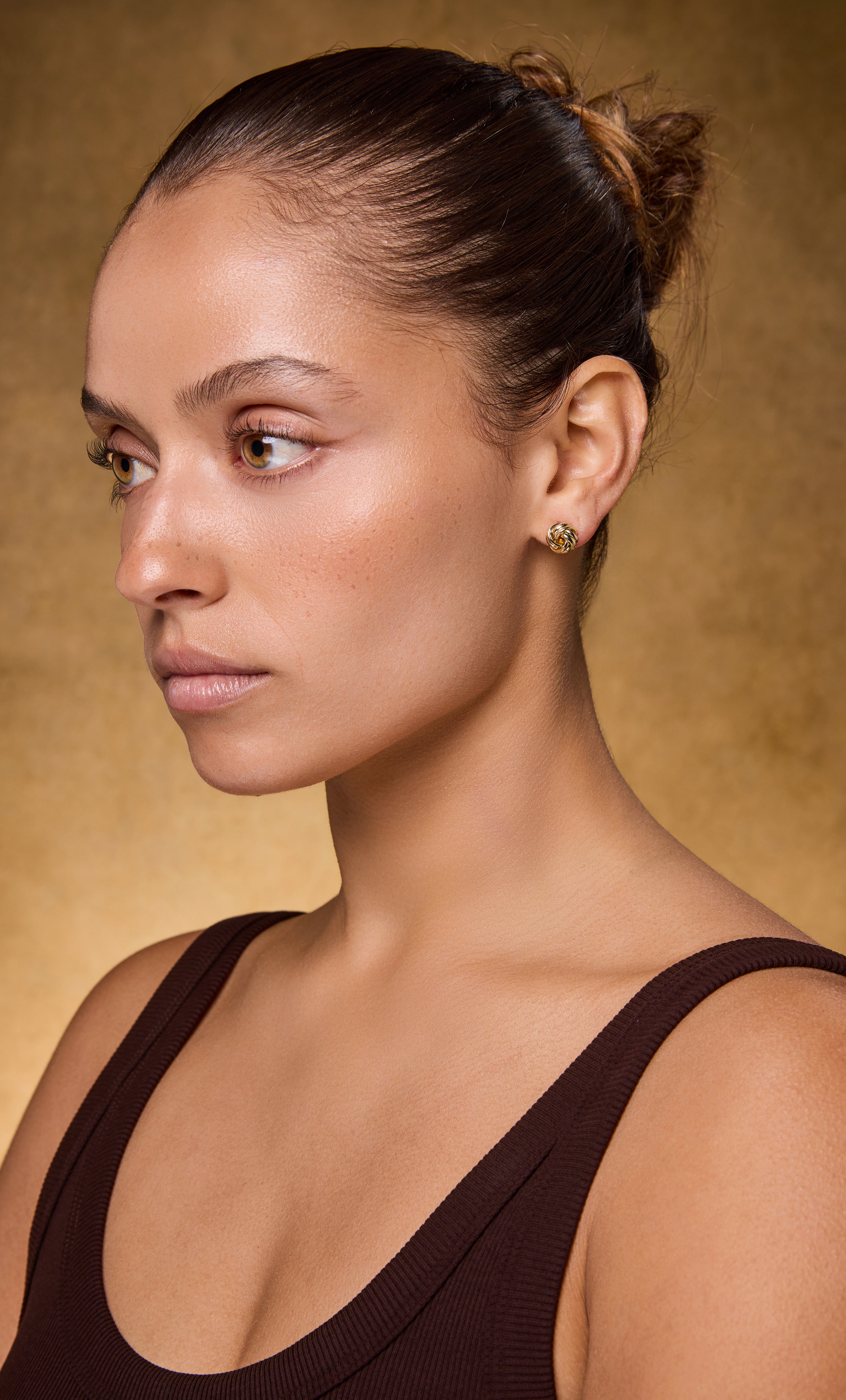 Woman wearing 14K gold fill dainty knot stud earrings from Tunik jewellery collection.