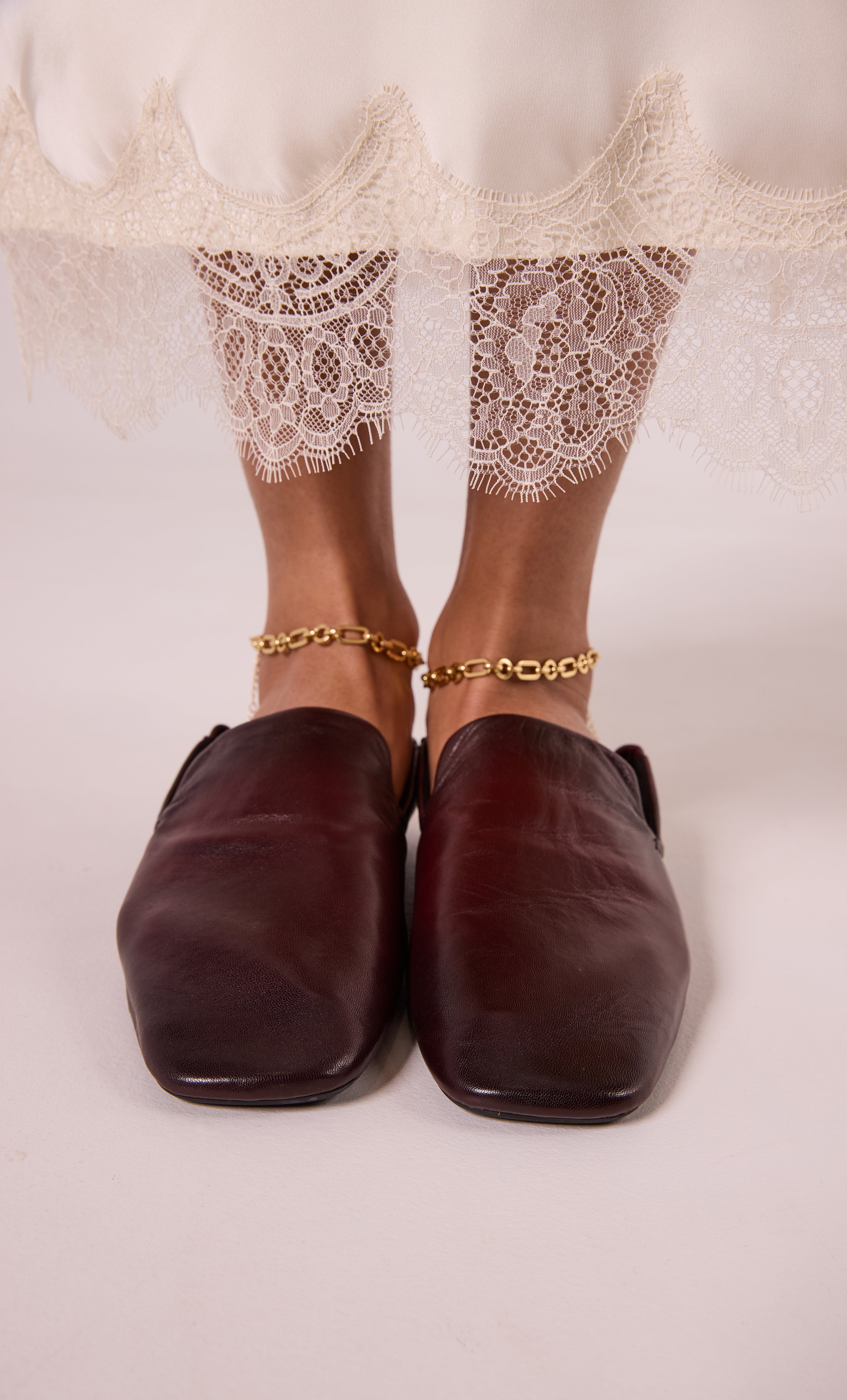 24K gold fill thick paper clip chain anklet by Tunik layered over lace-trimmed cream pants with brown leather shoes.
