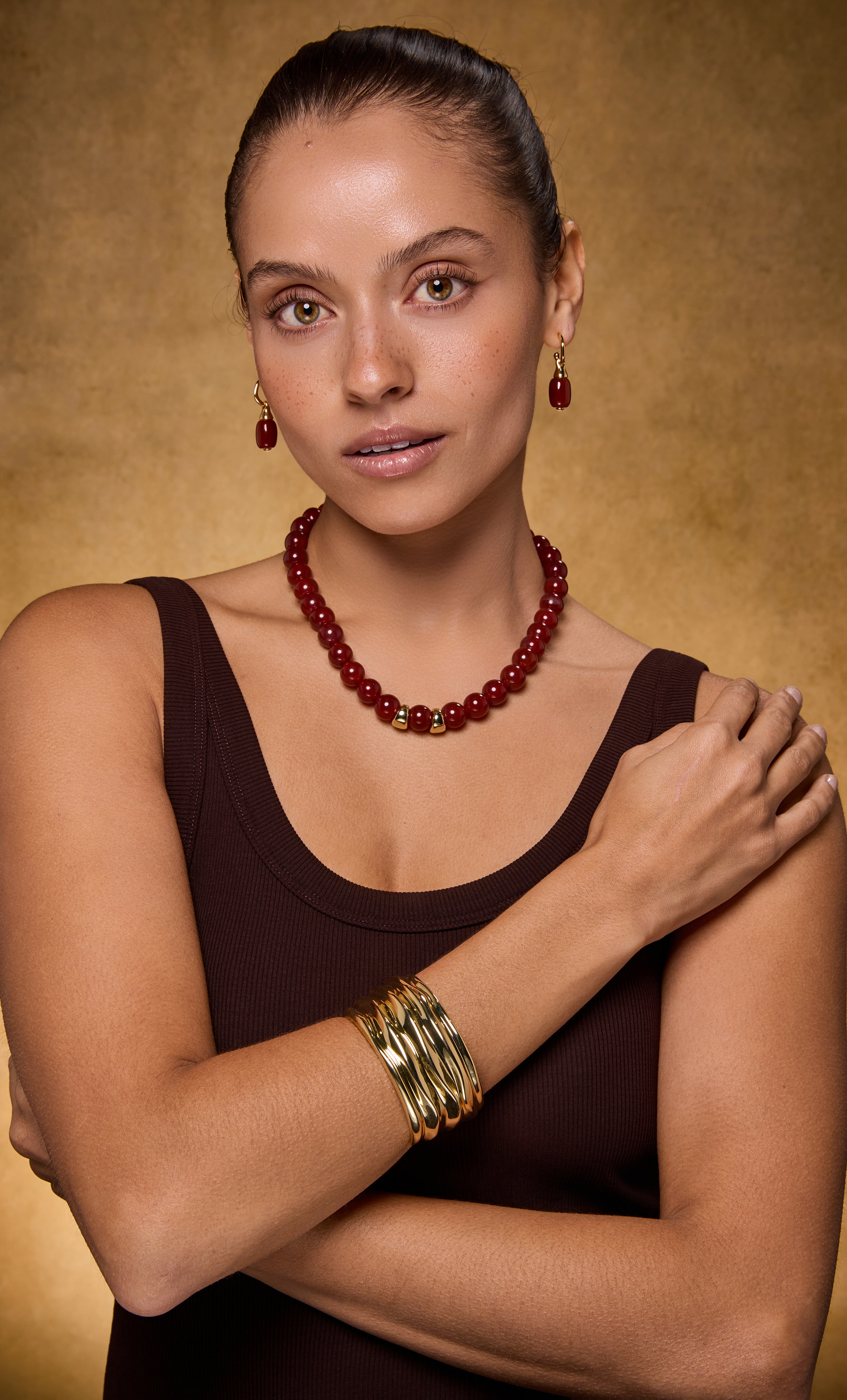 Gold fill ripple cuff bangle bracelet on model wearing red beaded Tunik necklace and earrings.
