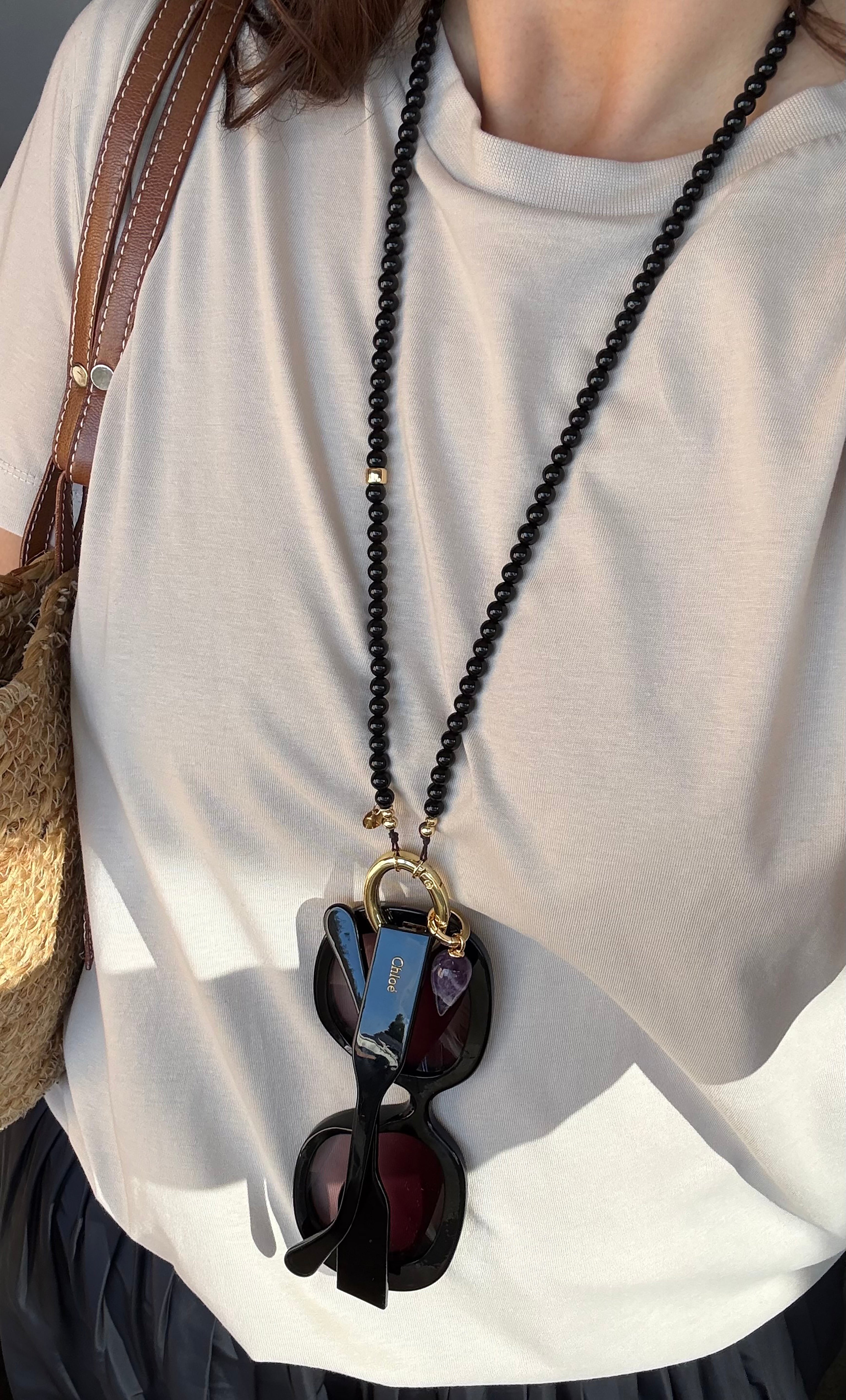 Black agate stone bead necklace with 14K gold fill clasp holding sunglasses and keys, worn with a beige top.