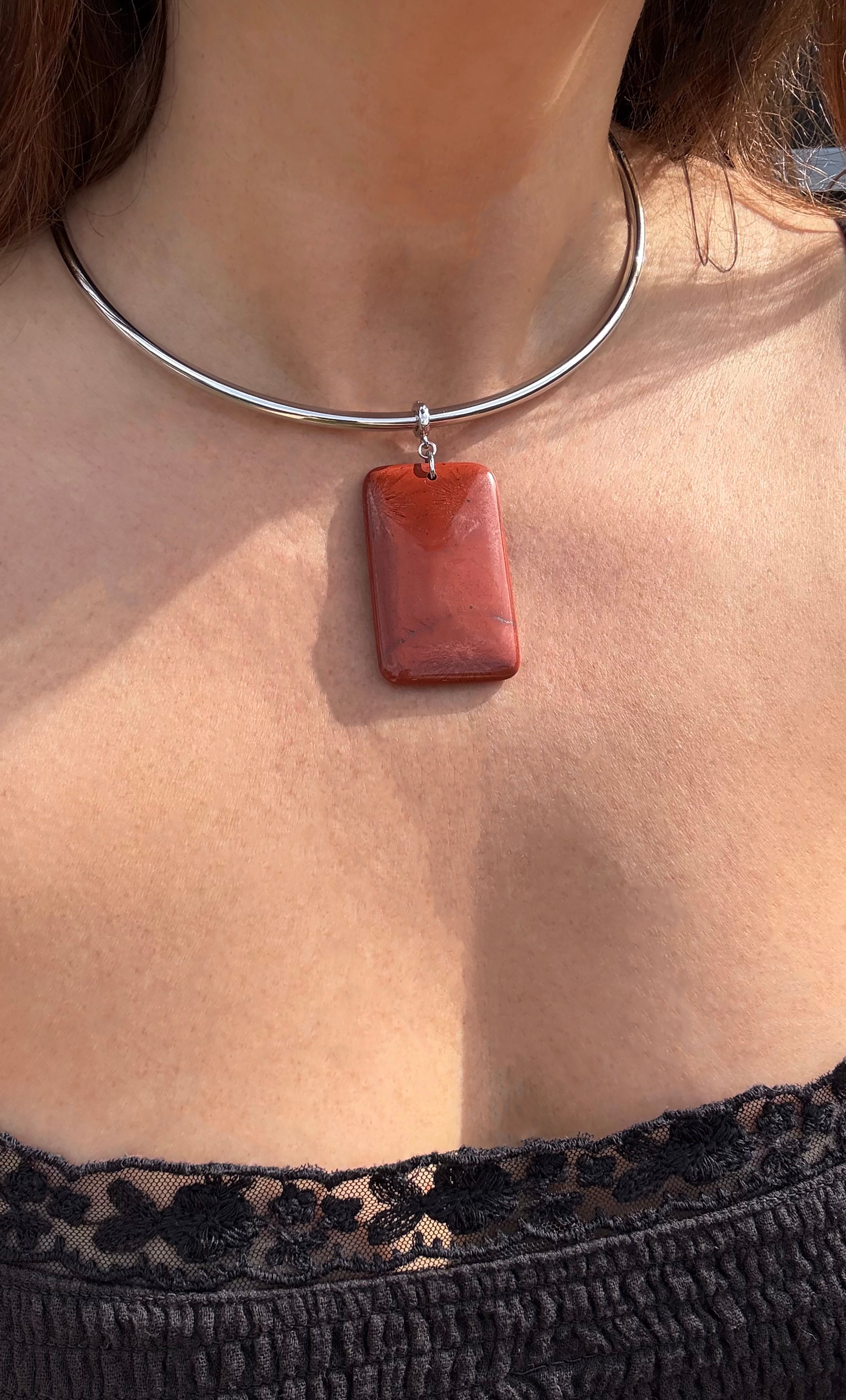 Silver collar necklace featuring a rectangular red jasper pendant with smooth edges, worn above black lace top.