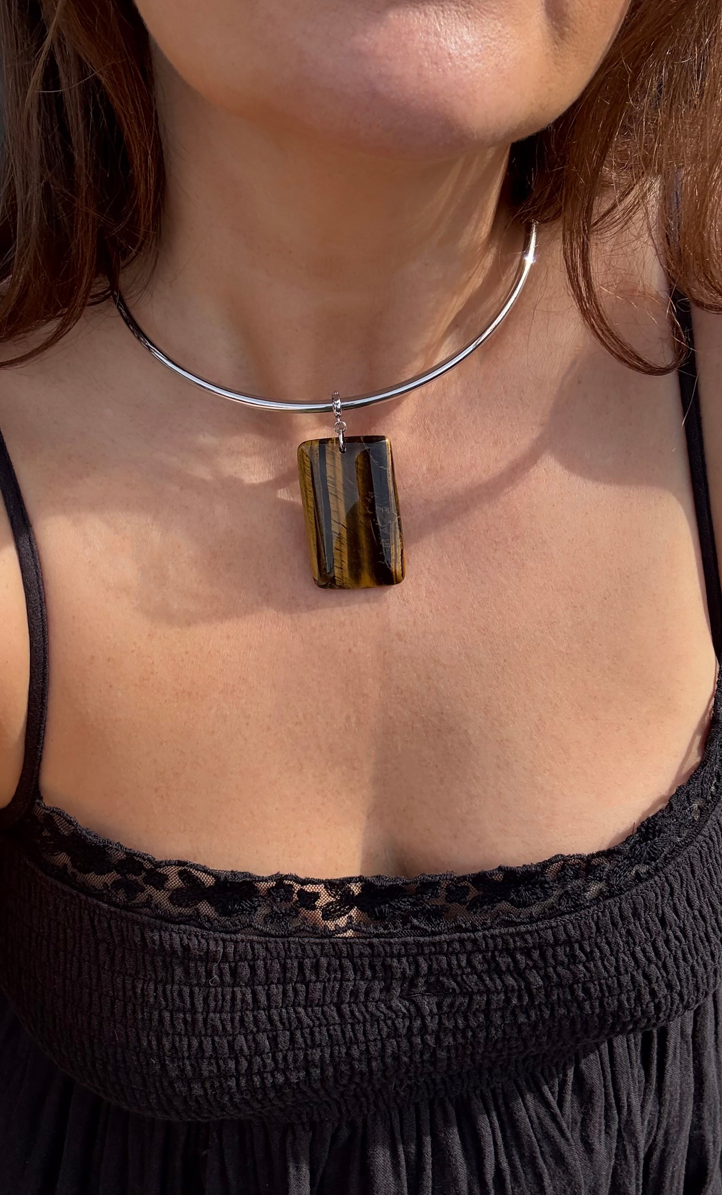 Silver collar necklace with rectangular tiger's eye stone pendant worn on bare neck.