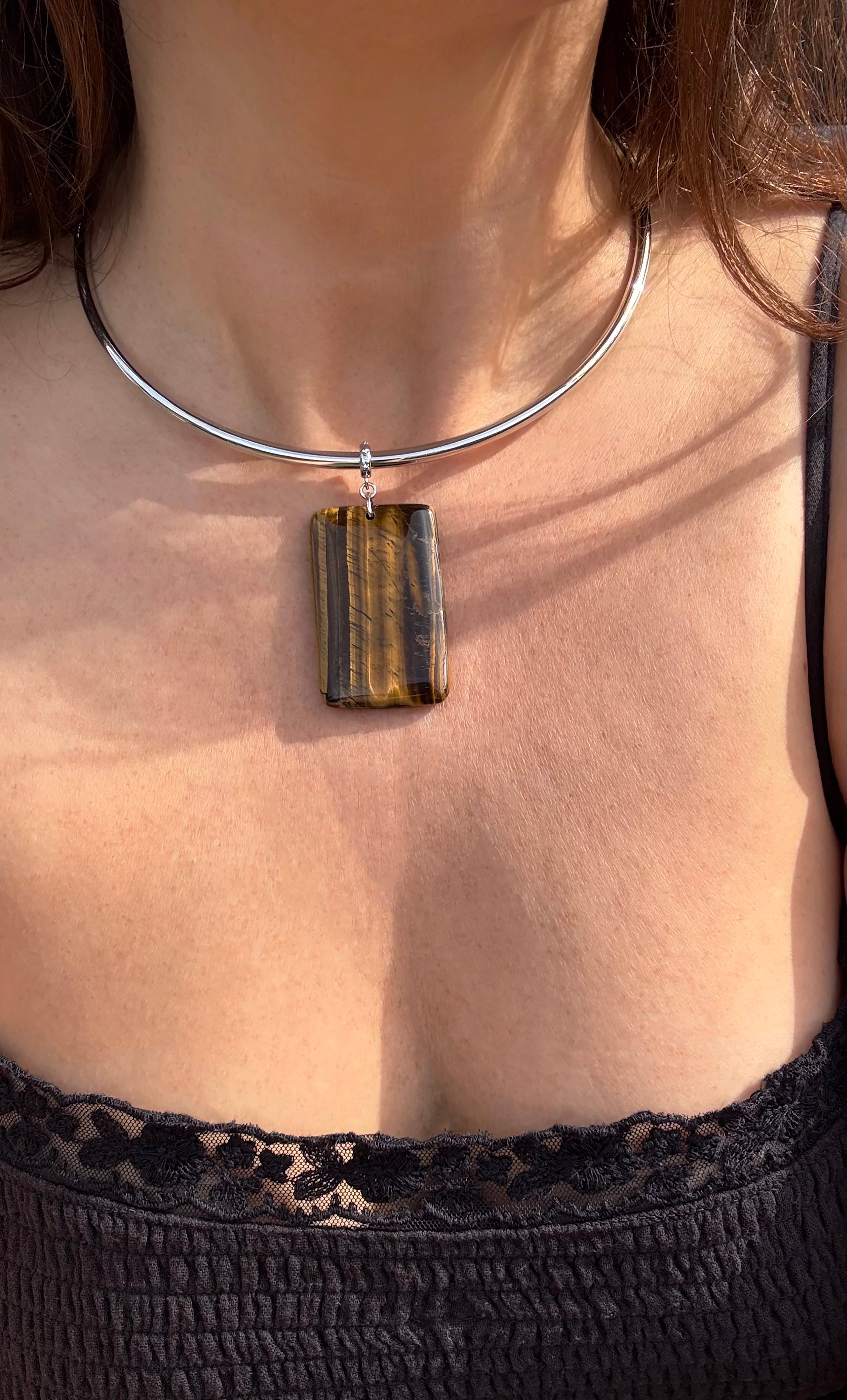 Silver collar necklace with rectangular polished tiger's eye pendant on a woman wearing black lace top.