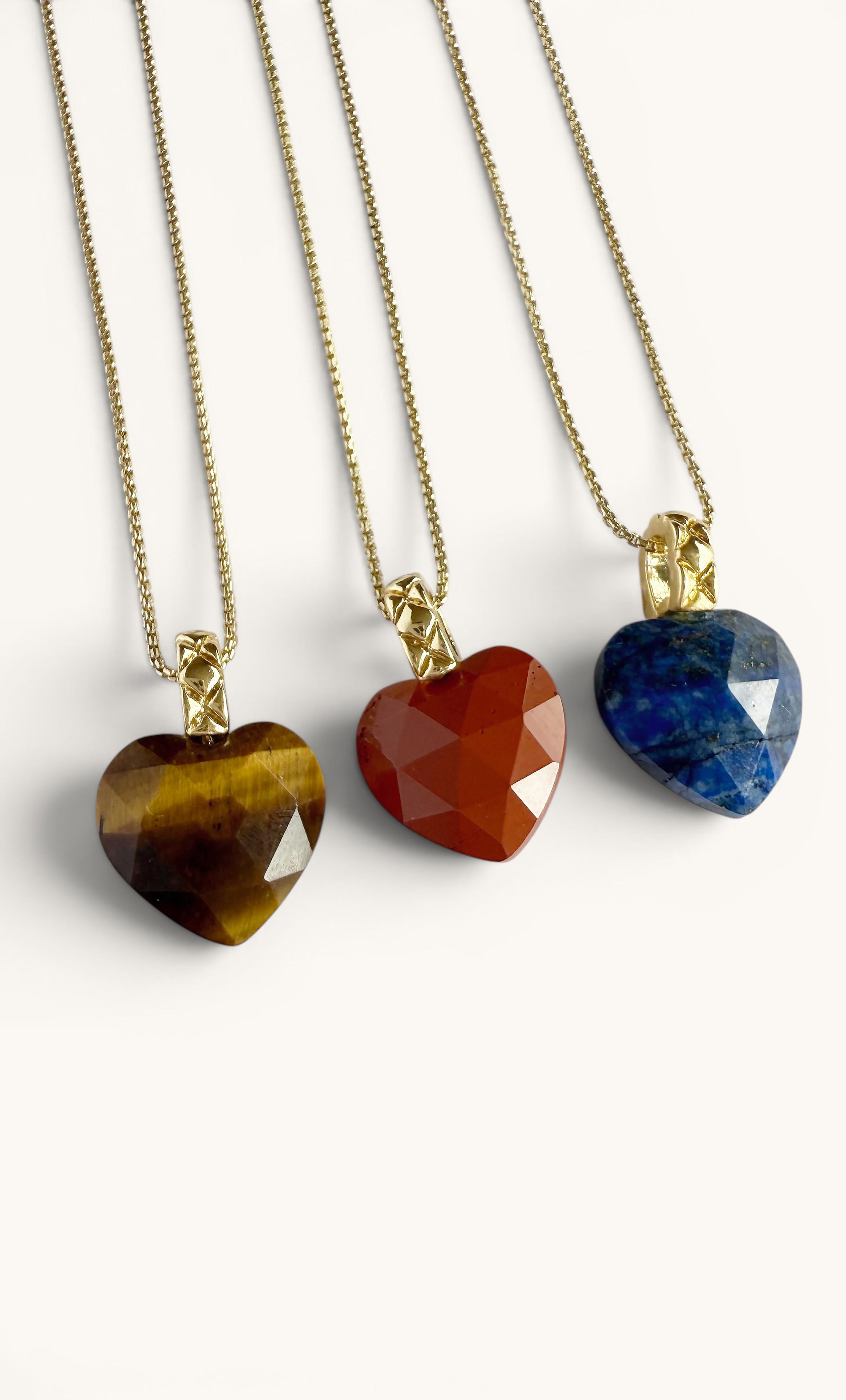 Three heart-shaped carved stone pendants in tiger's eye, carnelian, and lapis lazuli, each with 18K gold fill chains.