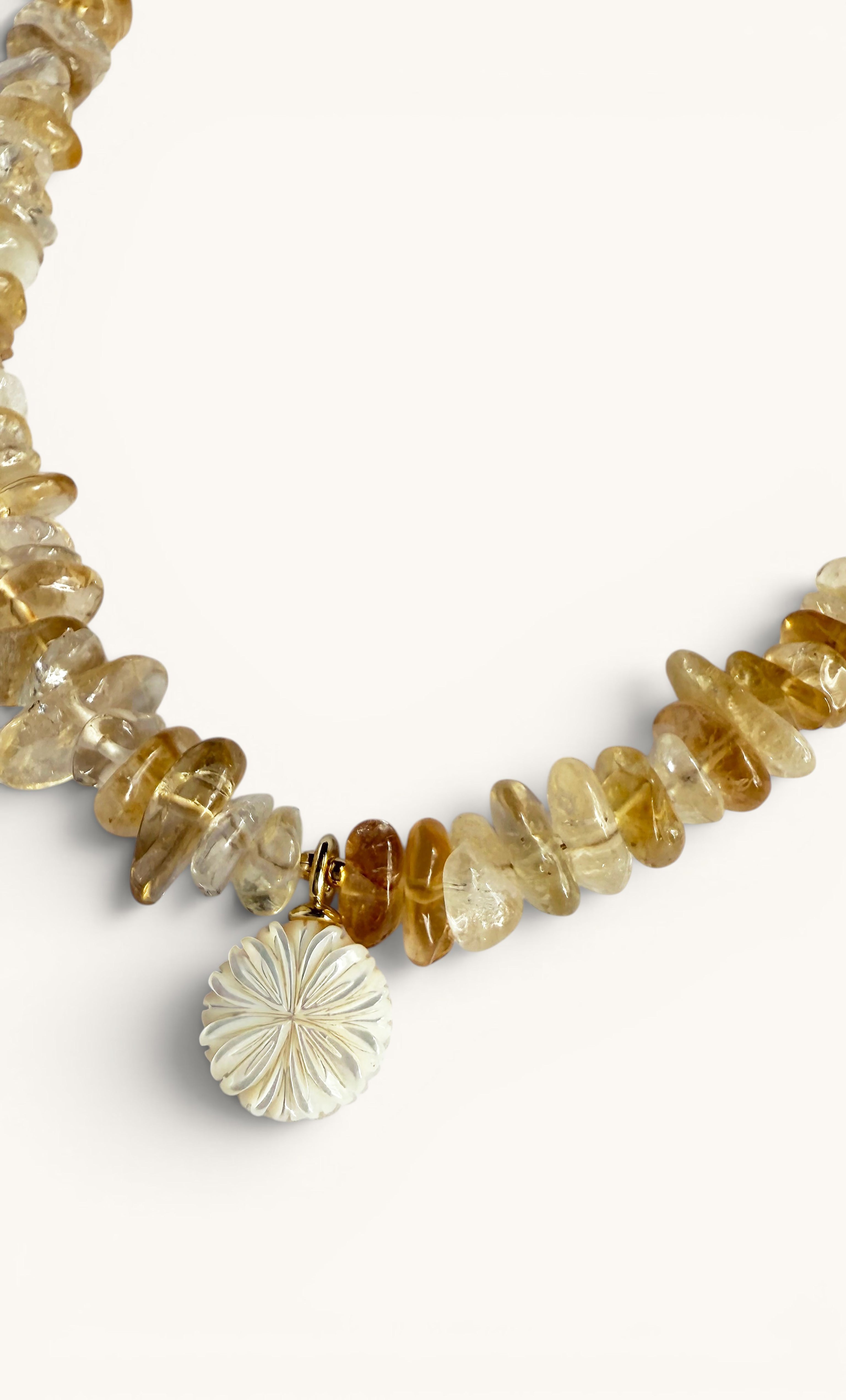 Gold-fill necklace featuring irregular yellow citrine stones and a white flower-carved pendant.