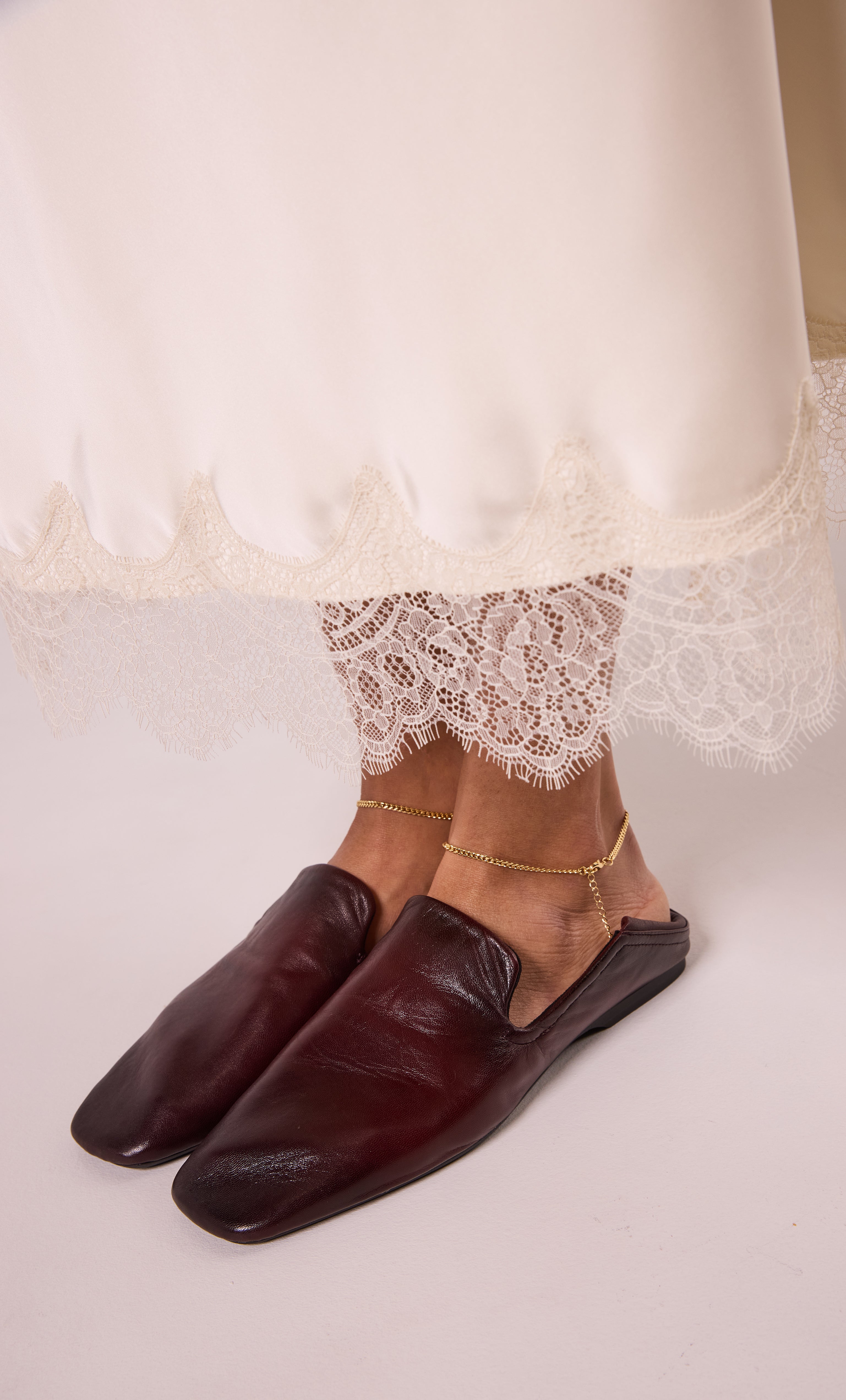 24K gold fill fine curb chain anklet by Tunik the Label styled with lace-trimmed dress and brown leather slip-on shoes,.