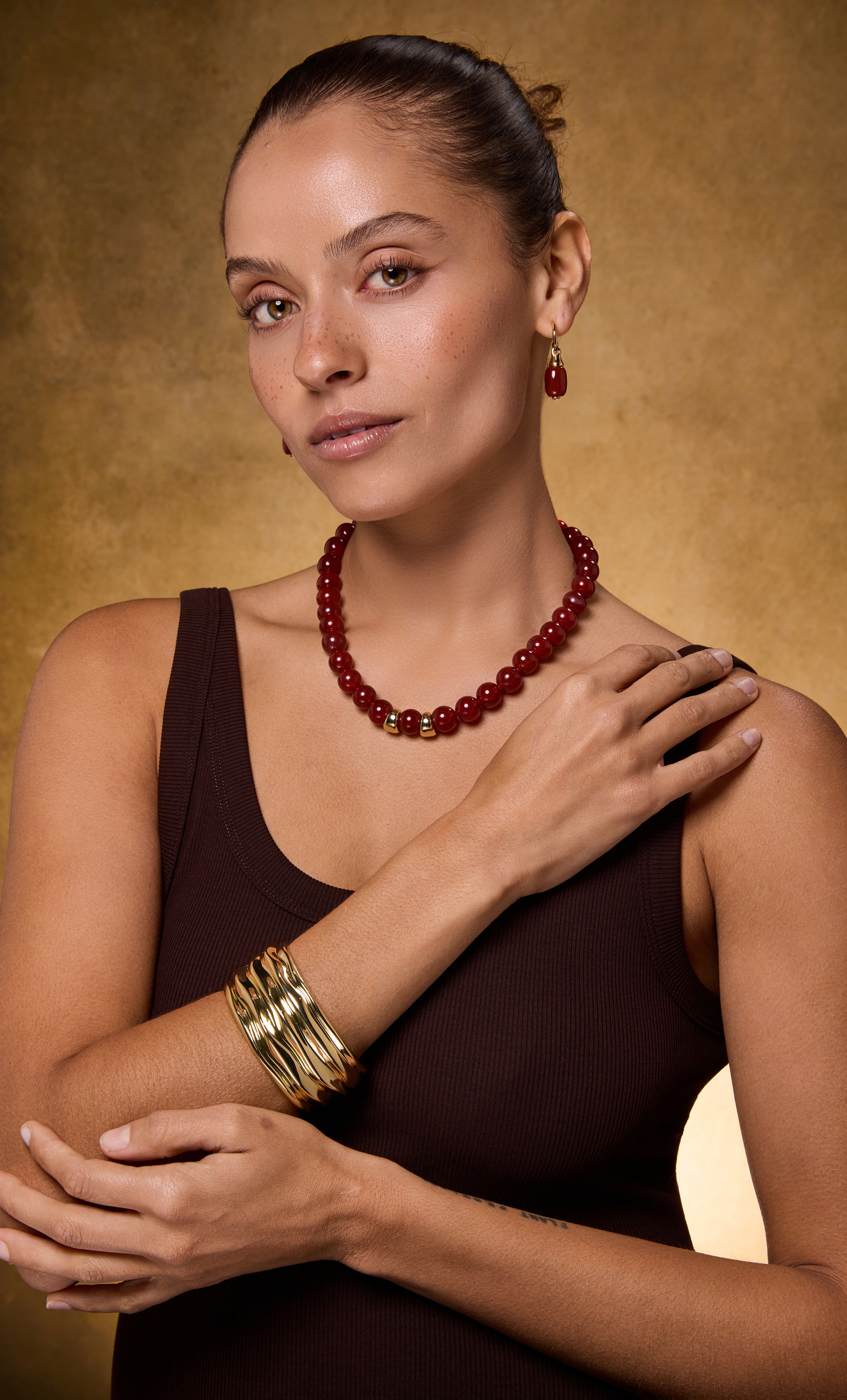Tunik 18K gold fill statement drop hoop earrings with carnelian red stones paired with matching gold necklace and bangles.