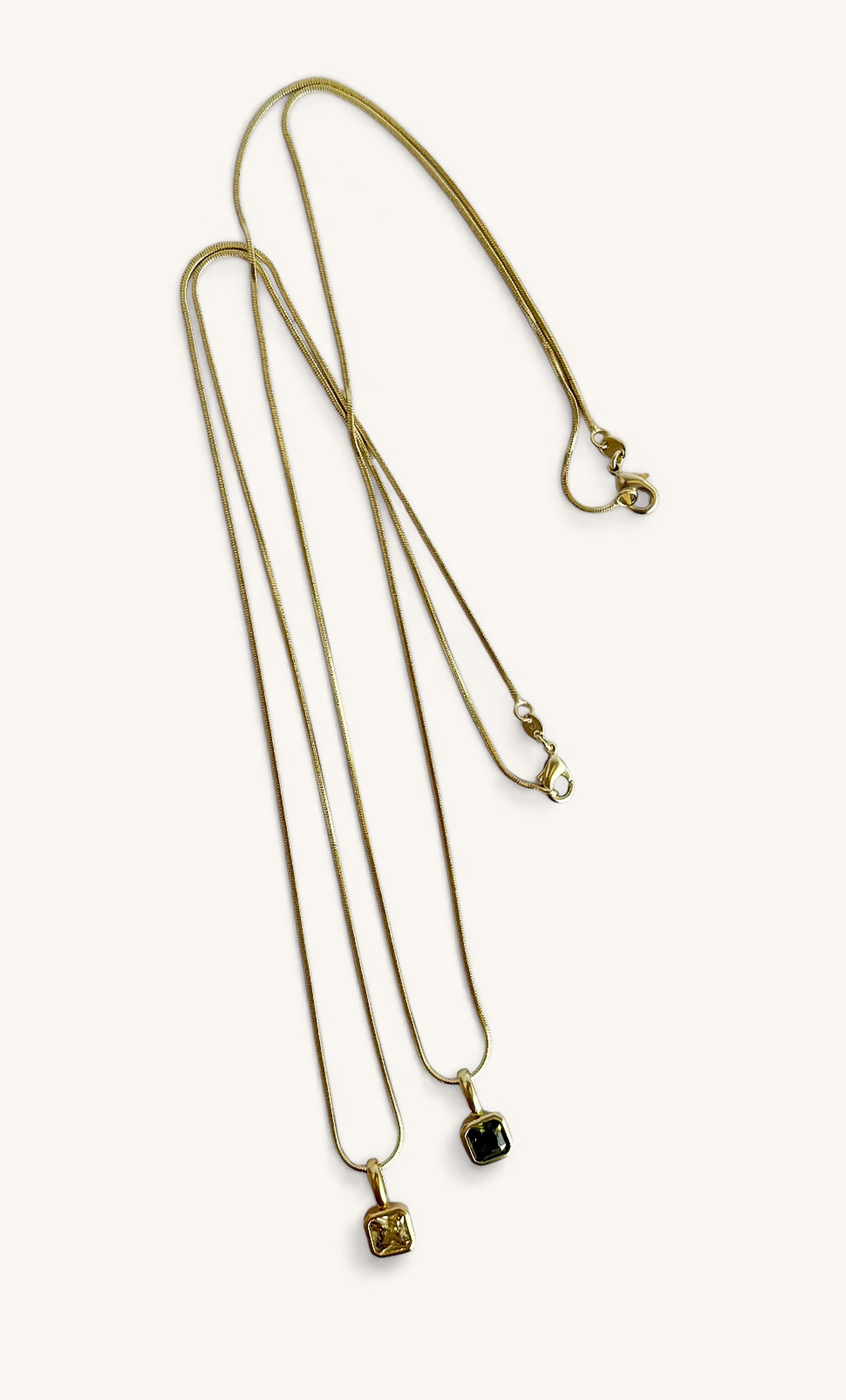Two 14K gold fill fine snake chain necklaces from Tunik The Label with square stone drop pendants in pale yellow and black.